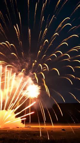 Vertical fireworks video launching golden shells over sandy field at night with sparks