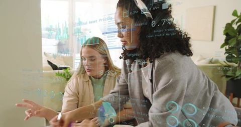 Two women collaborating with holographic data visualizations in modern home office