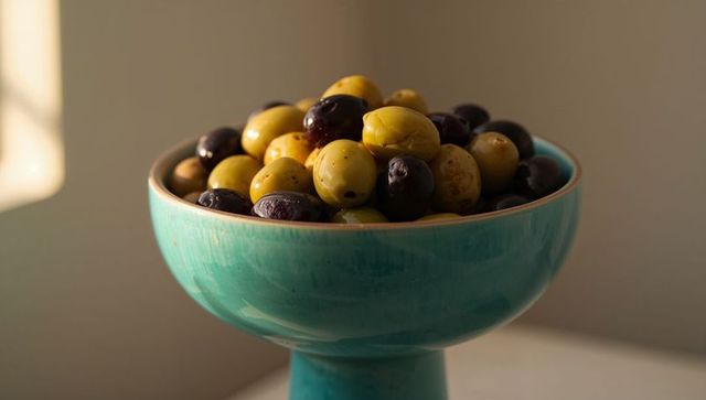 Turquoise footed bowl overflowing with green and black olives in warm sunlight
