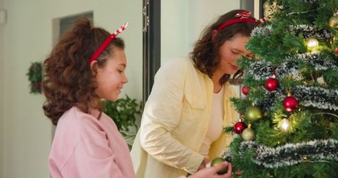 Mother and daughter decorating christmas tree with ornaments
