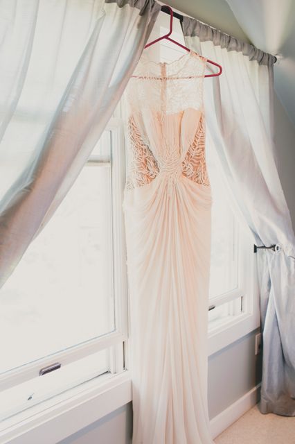 Lace wedding dress hanging by a brightly lit window, creating a romantic and elegant atmosphere. Ideal for use in wedding magazines, bridal shops, fashion blogs, or social media content related to weddings and bridal fashion.
