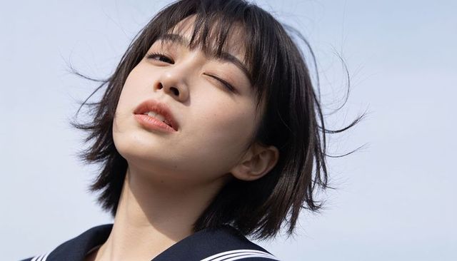 Windblown asian teen girl closeup portrait in sailor uniform closing one eye against sky