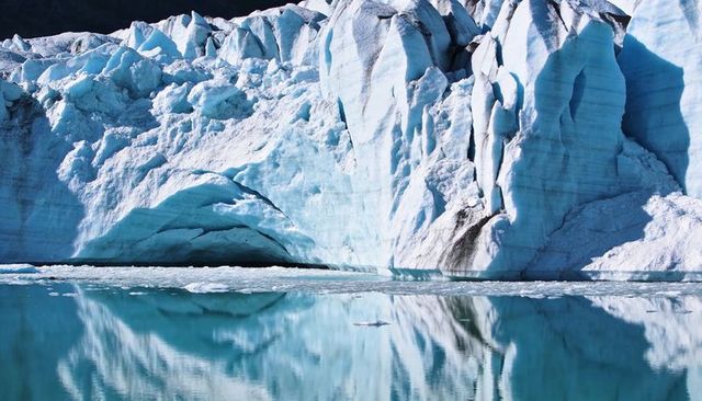 Towering blue glacier meeting calm meltwater fjord reflecting crevasses and ice arches