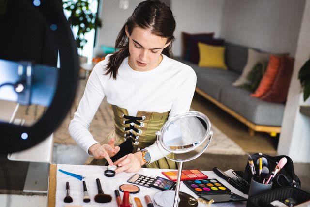 Caucasian woman preparing makeup in a studio, surrounded by various cosmetics and tools. Ideal for use in articles or advertisements about beauty, makeup artistry, small business ownership, and creative workspaces.