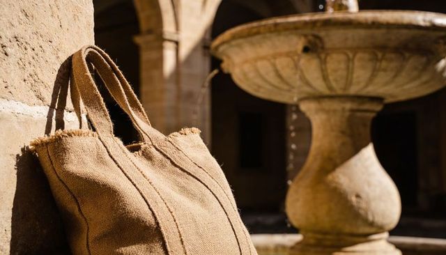 Leaning burlap tote bag catching sunlight on stone pillar beside carved fountain