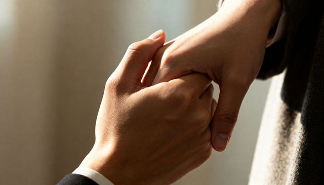 Suit-sleeved man holding loved one's hand in gentle cradle under warm directional light