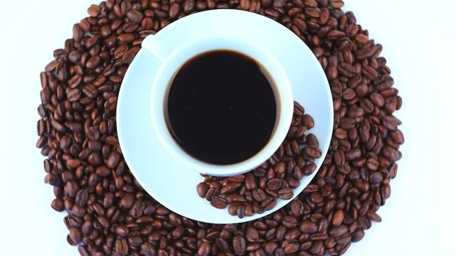 Top view of a white cup filled with black coffee on a bed of roasted coffee beans. Can be used for advertising coffee brands, illustrating coffee-related articles, or for promotional materials for cafés.