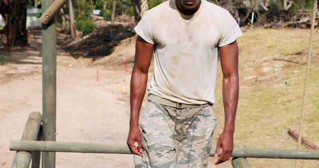 A young African American military man appears exhausted after a rigorous training exercise, with copy space. His dirt-stained shirt and fatigues suggest a high level of physical activity in an outdoor environment.