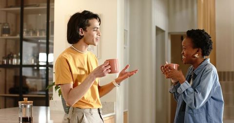 Diverse friends chatting over coffee in bright modern kitchen holding ceramic mugs
