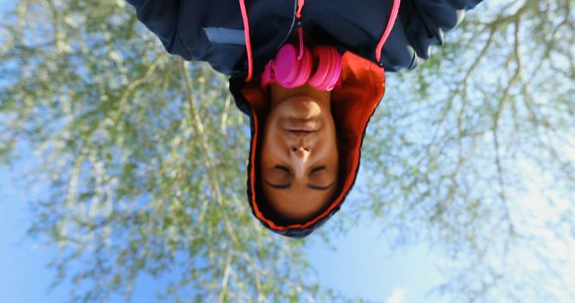 An African American teenage boy hangs upside down outdoors, with a playful expression and wearing headphones around his neck. Capturing a moment of youthful exuberance, the image conveys a sense of freedom and carefree adventure.