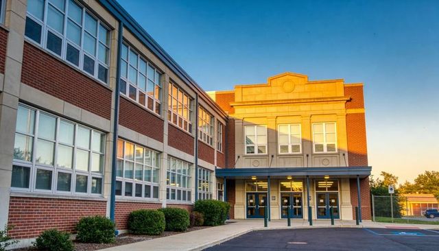 Golden-hour school entrance glowing on two-story brick building with canopy and columns