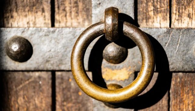 Glinting brass ring door knocker casting sharp shadow on weathered wooden door