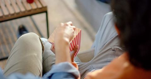 Friends sharing popcorn on sofa during cozy movie night at home casual relaxed moment