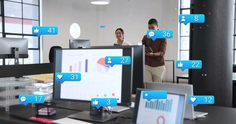 Open-plan workspace showing dashboards with social engagement icons, collaborating colleagues