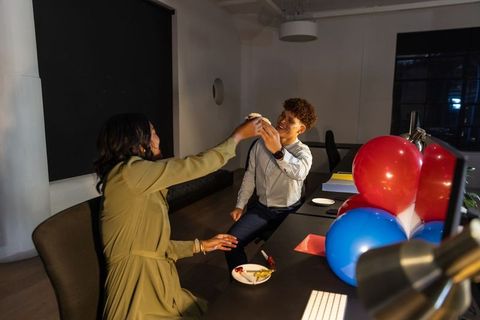 African american coworkers celebrating with cupcake and balloons at modern office desk