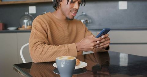 African american man checking smartphone in cozy cafe with latte and pastry