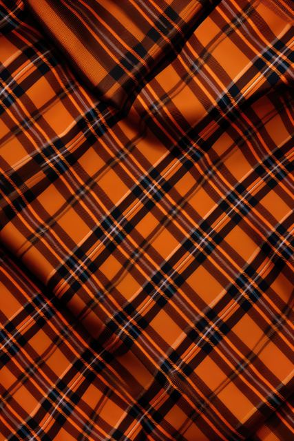Vivid bright orange tartan fabric featuring a classic check pattern. Applies as a stylish textile in clothing, fashion design, upholstery, and craft projects. Ideal for high-fashion accessories or traditional garments with a modern twist. Versatile textile suggests various creative applications in home decor and graphic design.