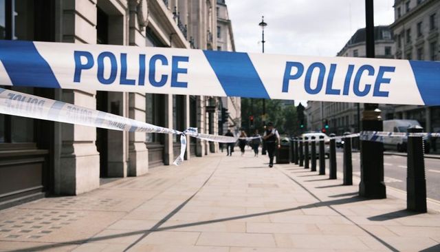 Blue-and-white police tape cordoning off urban sidewalk with officers, neoclassical facades