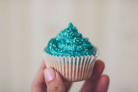 Hand holding blue frosted cupcake with sprinkles