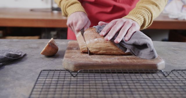 Person slicing fresh homemade bread on cutting board in kitchen. Ideal for cooking blogs, cooking tutorials, food magazines, or advertisements showcasing home-cooked meals and bread-making.
