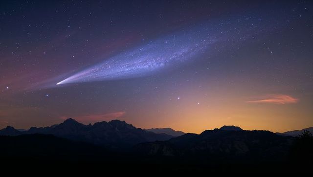 Streaking comet crossing twilight sky above mountain ridge with violet tail and milky way