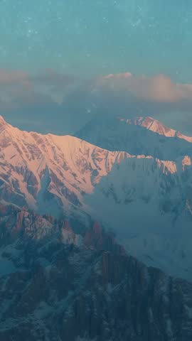 Vertical aerial panning revealing snowy alpine peaks at dawn with drifting light flecks