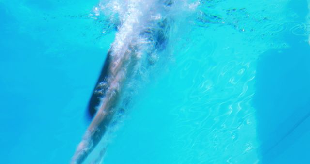 This dynamic shot captures a swimmer diving underwater with motion blur, emphasizing speed and power. Ideal for use in projects related to swimming, athletics, fitness, competitive sports, or promotional materials for swimming pools and aquatic centers. The bright blue water backdrop enhances the sense of freshness and activity.