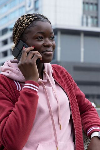 Teen african american female talking on phone in city wearing maroon jacket, pink hoodie