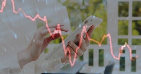 Hands Using Tablet for Mobile Trading with Fluctuating Red-Orange Stock Chart Overlay