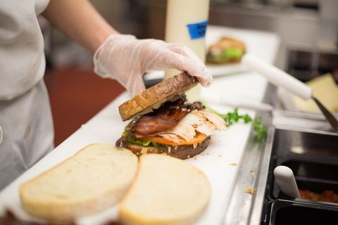 Chef assembling turkey and bacon sandwich with lettuce and tomato on whole grain bread