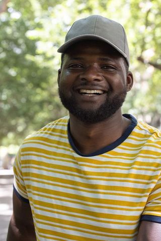 Smiling man wearing gray cap and yellow striped shirt enjoying sunlit park portrait