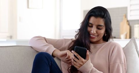 Smiling Woman Relaxing on Sofa Using Smartphone in Cozy Living Room