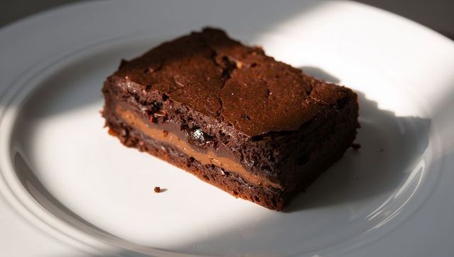 Decadent caramel-stuffed fudgy brownie slice sitting on white plate in soft light