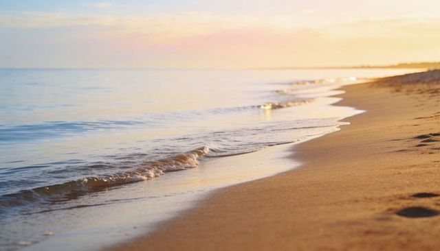 Sunrise waves lapping golden sandy shoreline with wet reflections and lone footprints