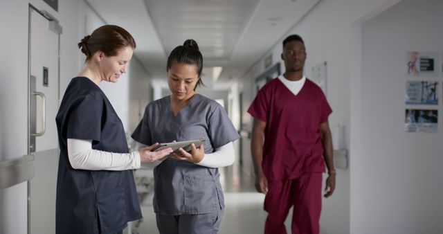 Healthcare professionals collaborate in a hospital corridor, discussing patient information on a tablet. This image highlights teamwork in the medical field, ideal for articles, blogs, or websites focusing on healthcare, medical teamwork, hospital environment, or patient care discussions.