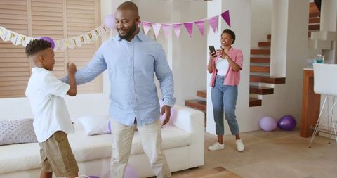 African American family celebrating at home, father fistbumping son, mother filming phone