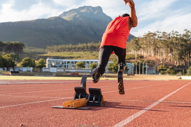Rear view of fit, biracial disabled male athlete at an outdoor sports stadium, starting sprint from starting blocks on race track wearing running blades. Disability athletics sport training.