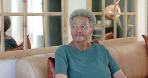 Senior african woman sitting on sofa looking contemplative and peaceful in living room