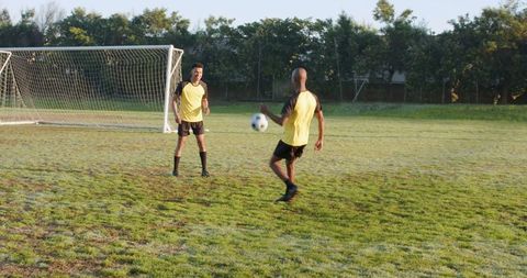 Teammates practicing soccer skills on field in yellow bibs