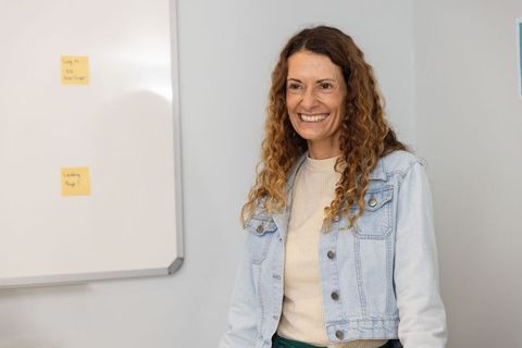 Smiling professional woman presenting in modern office classroom with whiteboard notes