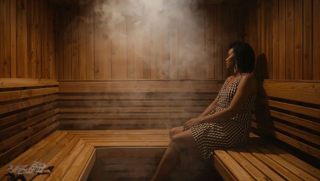 Woman with braids relaxing in steam-filled wooden sauna bench, warm amber wellness