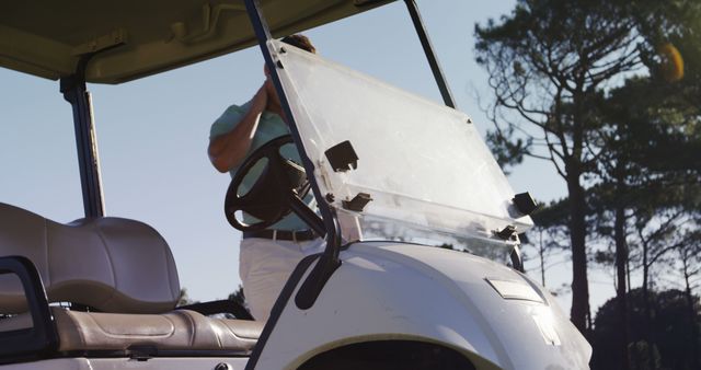 Golfer preparing on a golf cart, getting ready for a day at the course on a sunny day. Ideal for use in marketing materials for golf courses, sports equipment, outdoor activities, and leisure lifestyle. Perfect for illustrating athletic preparation and recreational activities.