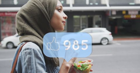 Young Woman in Hijab Enjoying Snack with Social Media Engagement