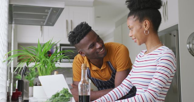 Image of happy african american couple cooking together in kitchen with tablet. love, relationship, togetherness and spending quality time at home.