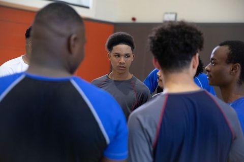 African american teen athletes huddling and listening during indoor basketball practice