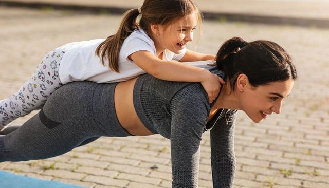 Mother daughter plank workout with child on back outdoor family fitness and playful bonding