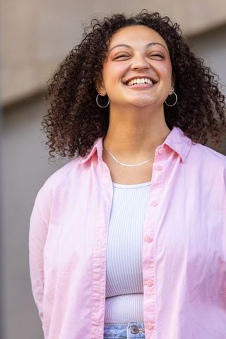 Laughing young woman in pastel pink shirt with curly hair and hoop earrings, candid portrait