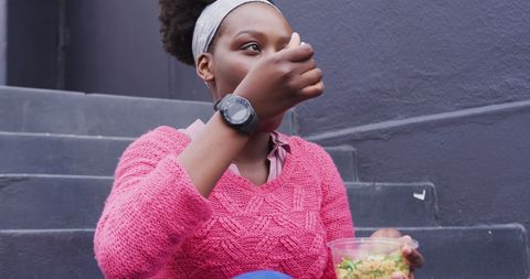 Young woman eating salad outdoors on city stairs