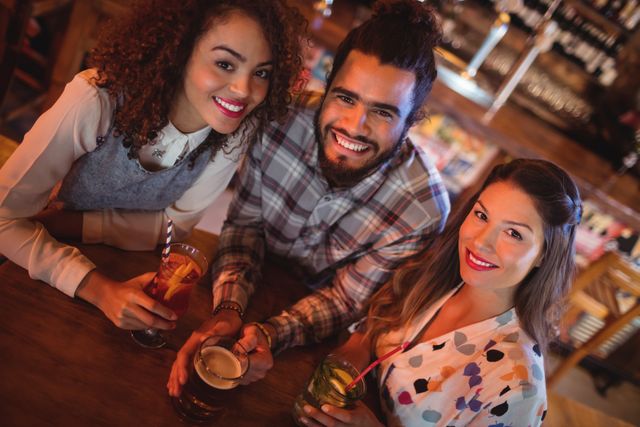 Group of young friends enjoying drinks at a pub, smiling and looking at the camera. Ideal for use in advertisements for bars, pubs, or social events, as well as articles about nightlife, friendship, and leisure activities.
