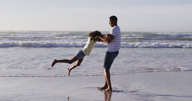 Father joyfully spinning daughter on beach with gentle waves and setting sun. Ideal for use in family vacations, summer fun, parent-child bonding, outdoor activities, and lifestyle promotions.